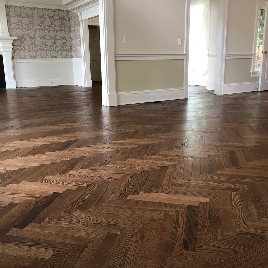 Herringbone pattern dark brown wood flooring in a room with white wainscoting.