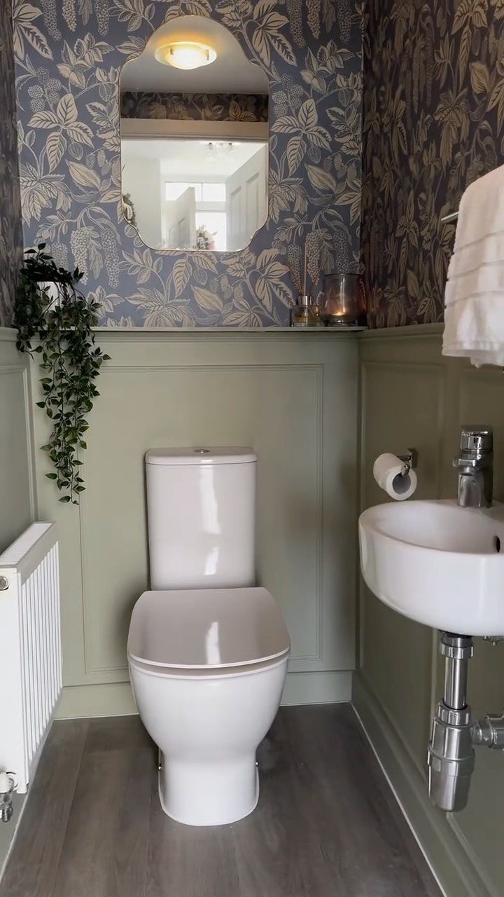 Sage green wainscoting paired with blue floral wallpaper in a small bathroom with a white toilet.