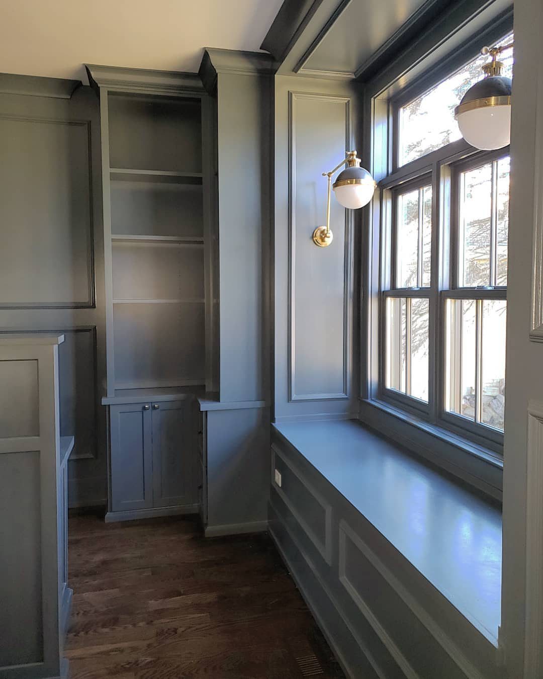 Gray painted wainscoting on walls, built-in shelving, and a window seat in a room.