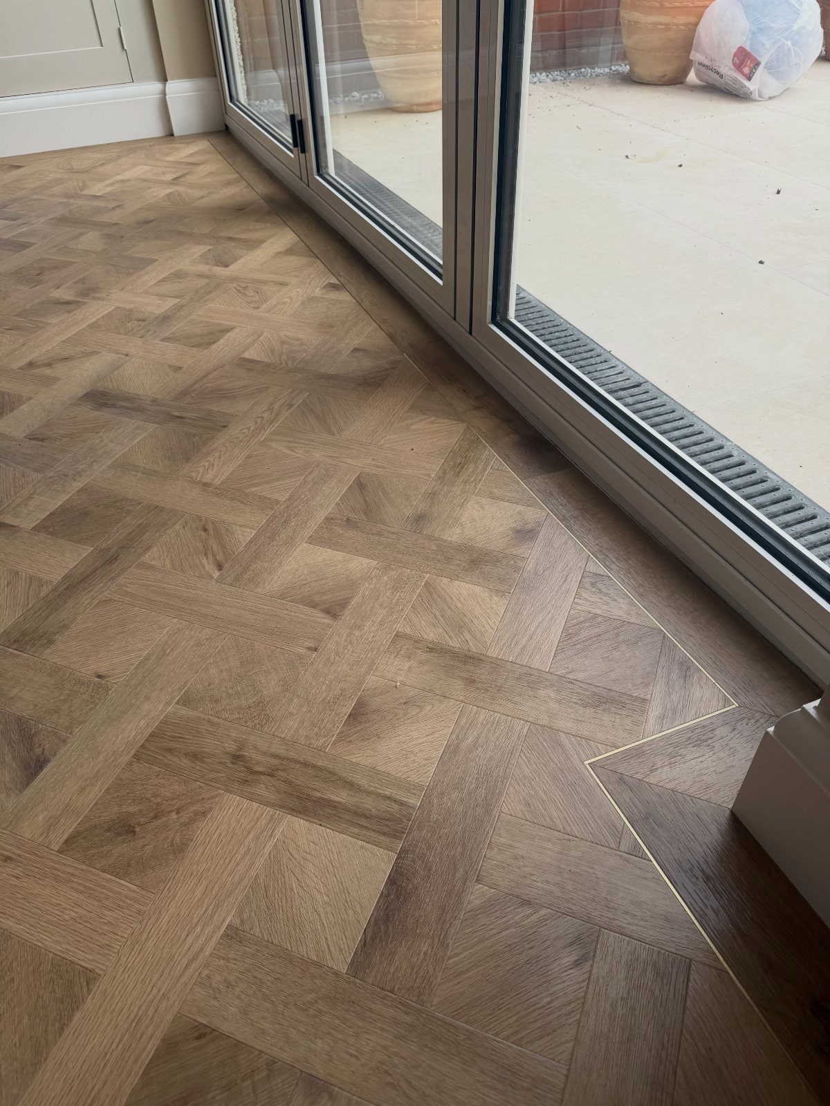 Basket weave pattern wooden parquet flooring next to a glass sliding door frame.