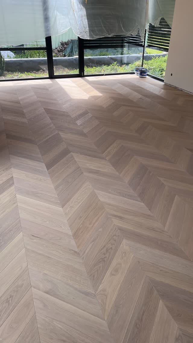 Light brown hardwood floor planks arranged in a sharp chevron pattern in a bright room.