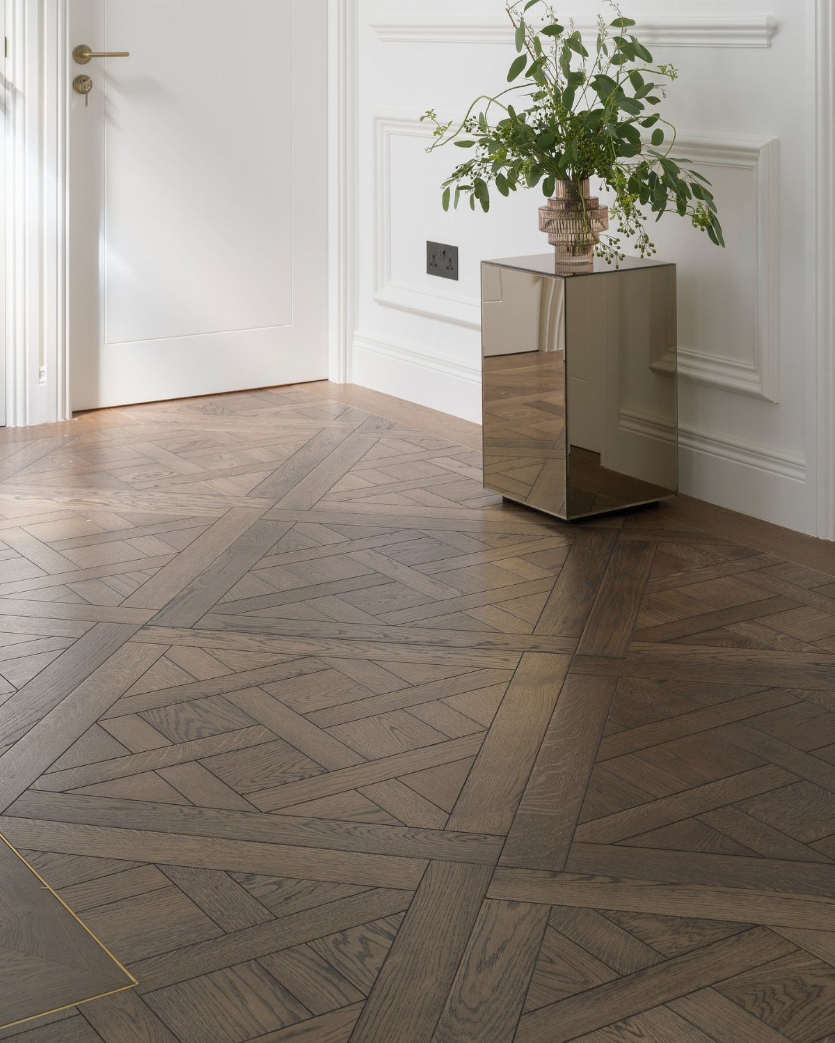 Intricate Versailles parquet hardwood flooring with geometric patterns in a bright room with white walls.