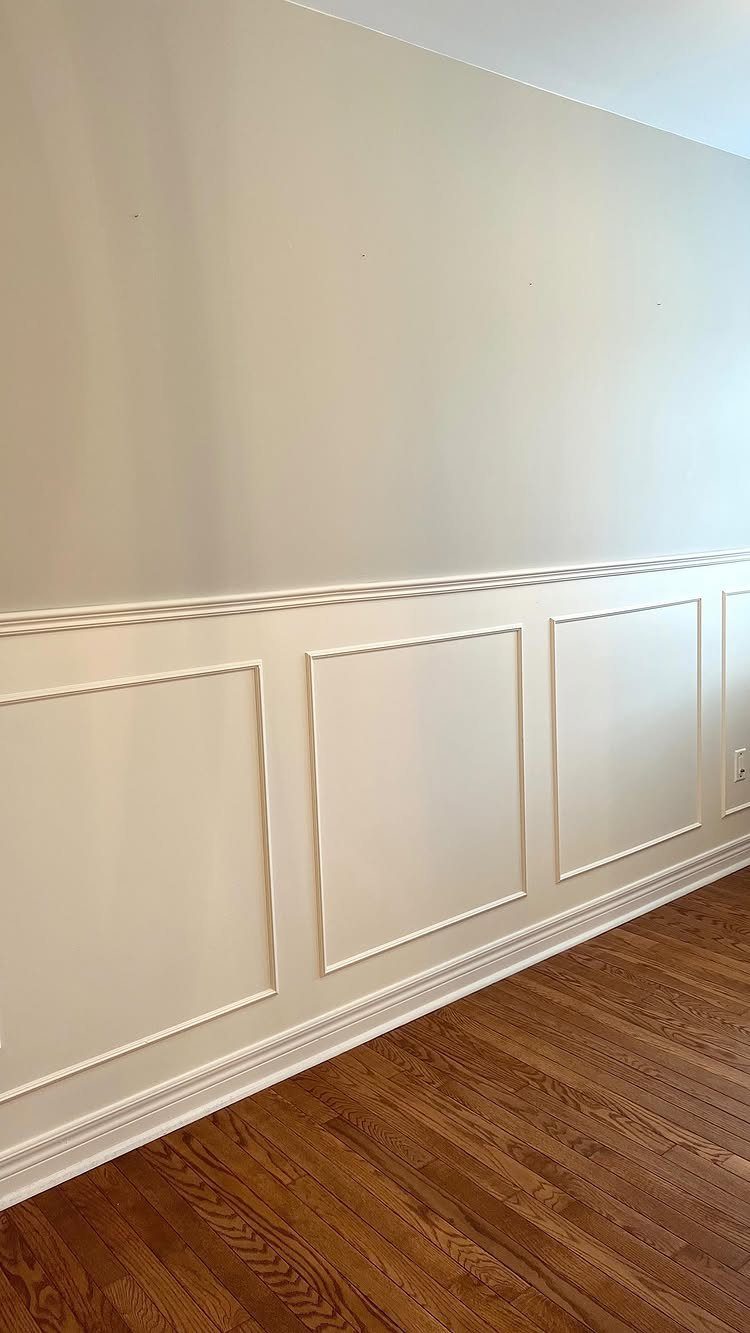 White wall with decorative picture frame molding and a horizontal chair rail above hardwood floors.