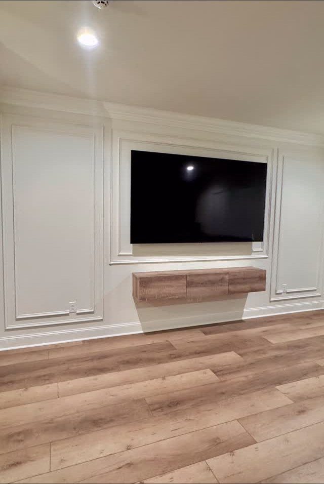 White accent wall with decorative picture frame molding surrounding a mounted television and wooden console.