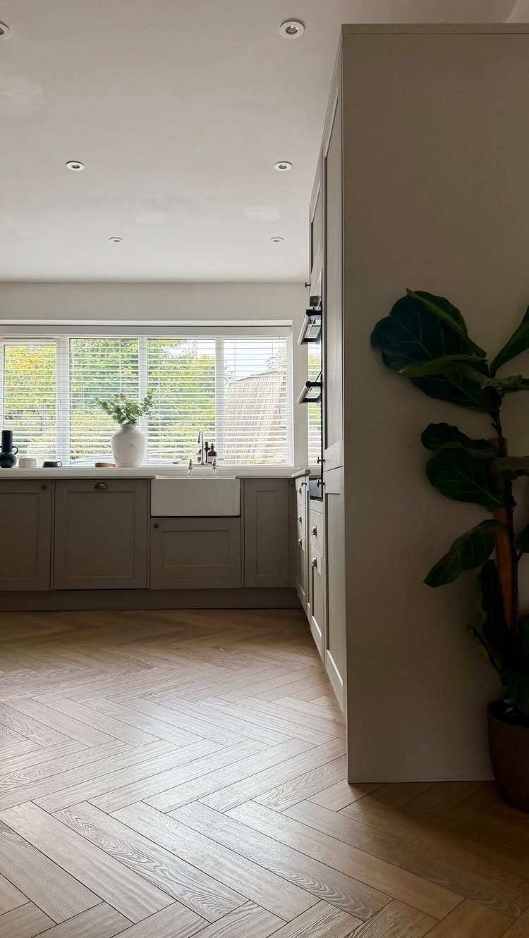 Light wood herringbone flooring in a modern kitchen with grey cabinets and a white sink.