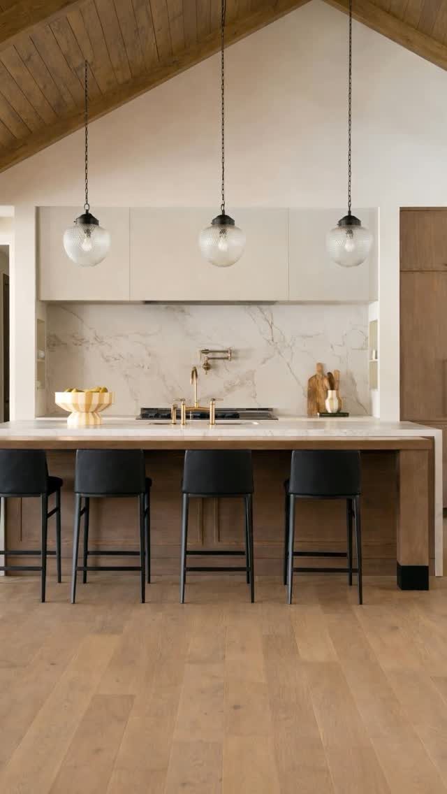 Light-colored wide plank hardwood flooring in a modern kitchen with a large island and pendant lights.