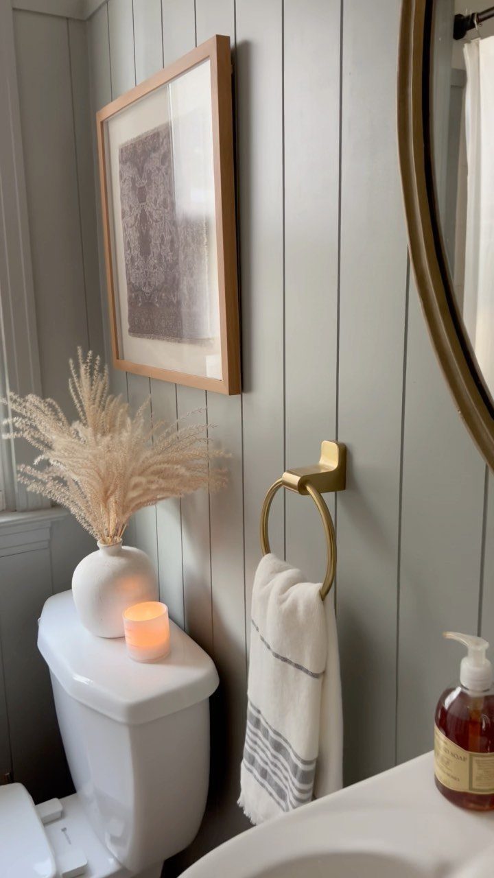 Light gray vertical shiplap wall in a bathroom with gold accents and dried pampas grass.