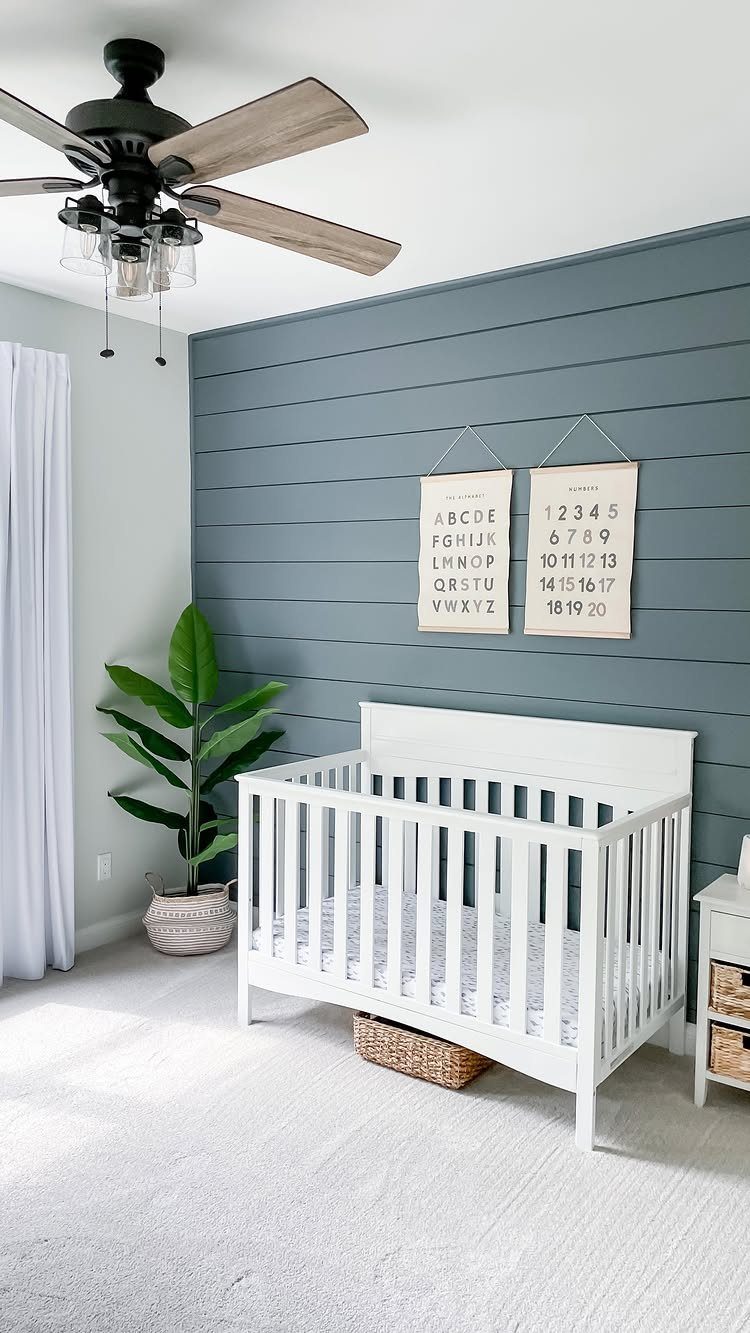 White baby crib positioned against a blue-grey shiplap accent wall in a bright nursery.