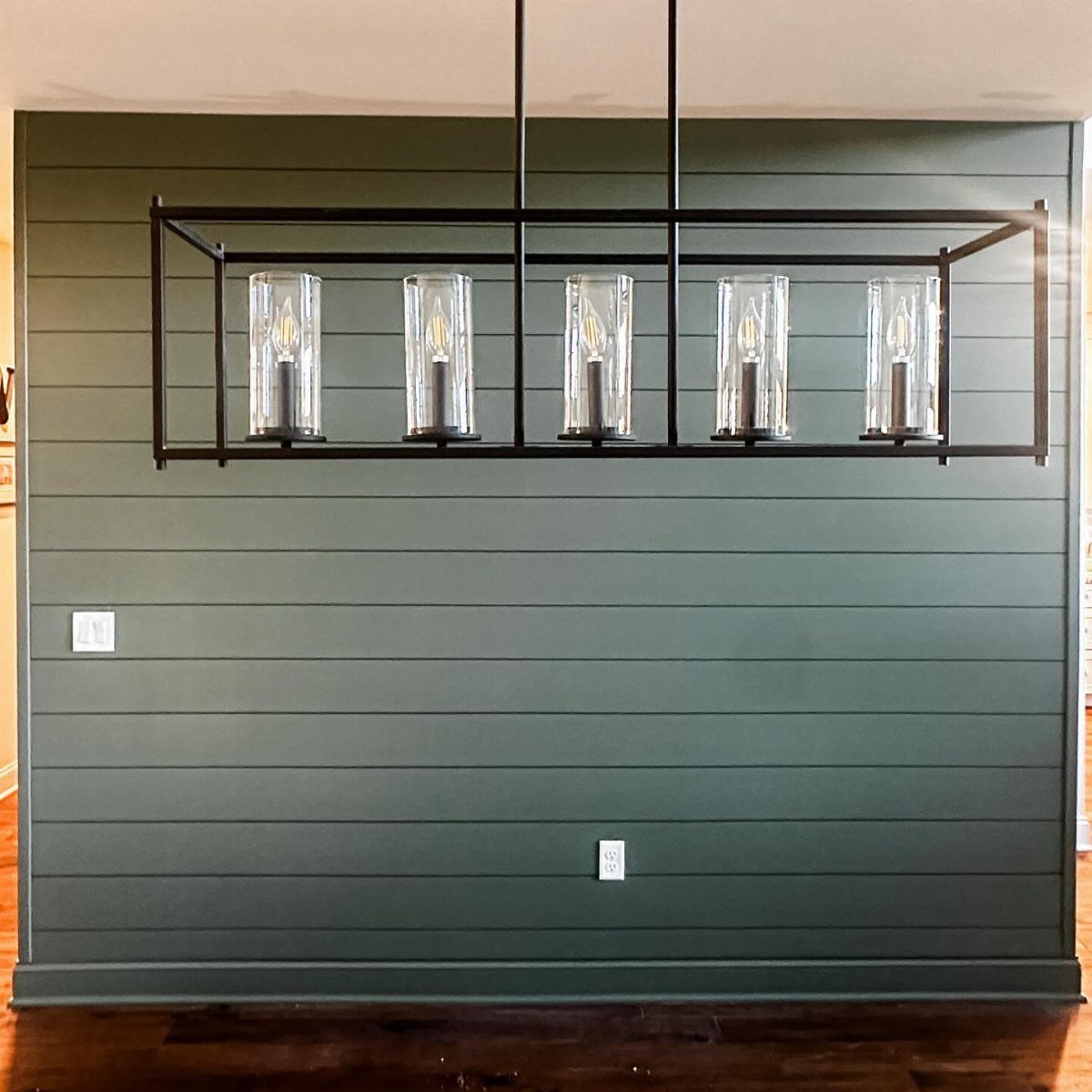 Dark green horizontal shiplap accent wall with a modern black linear chandelier hanging in front.