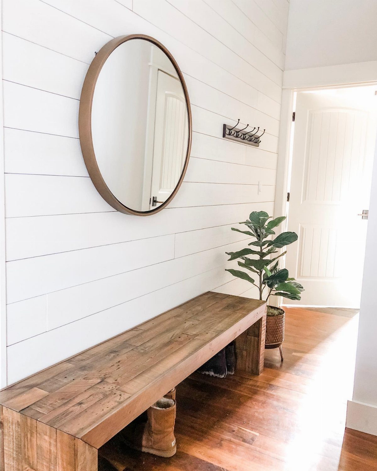 White shiplap accent wall with a round mirror and wooden bench in a bright entryway.