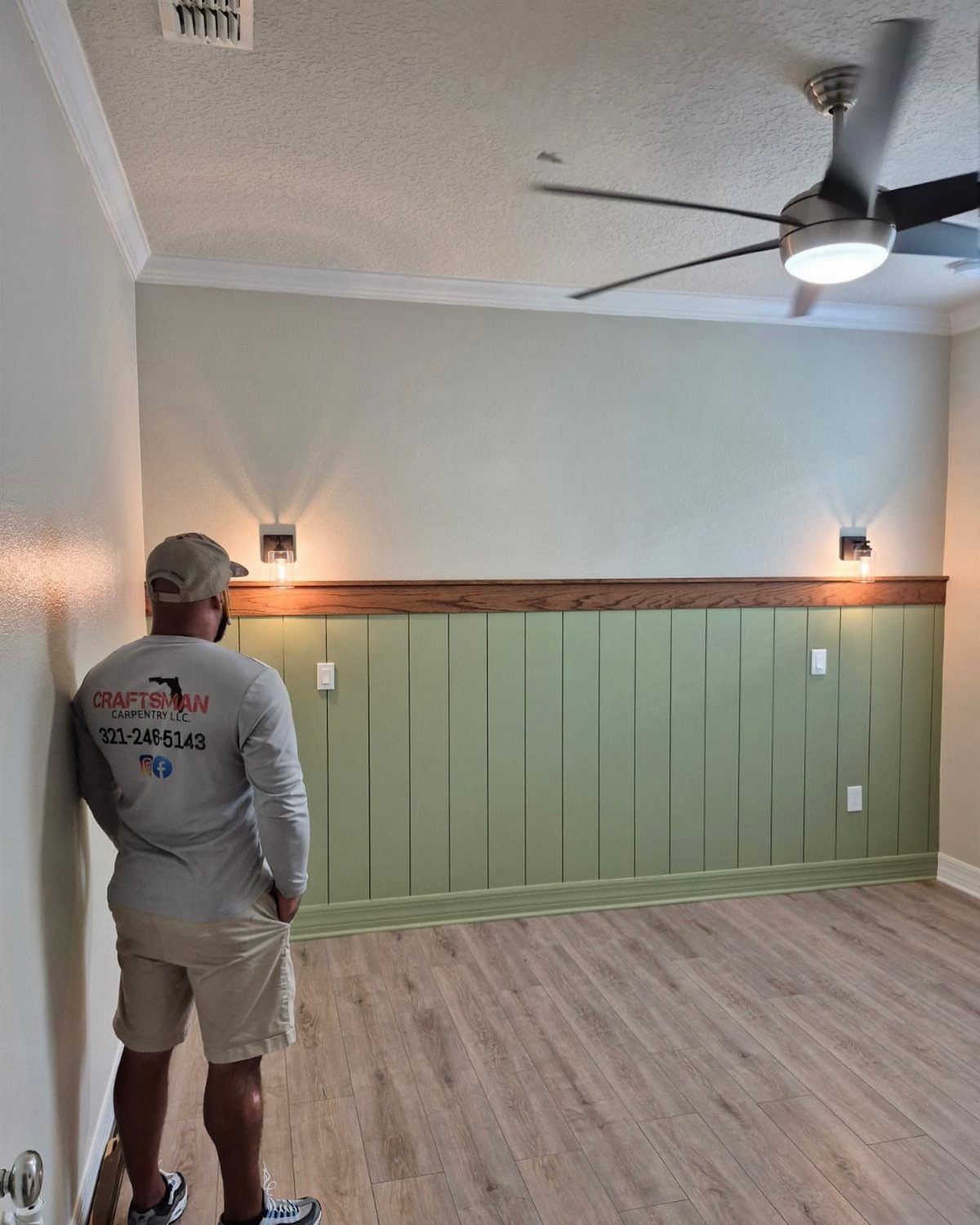 A man looking at a sage green vertical paneling half shiplap accent wall.
