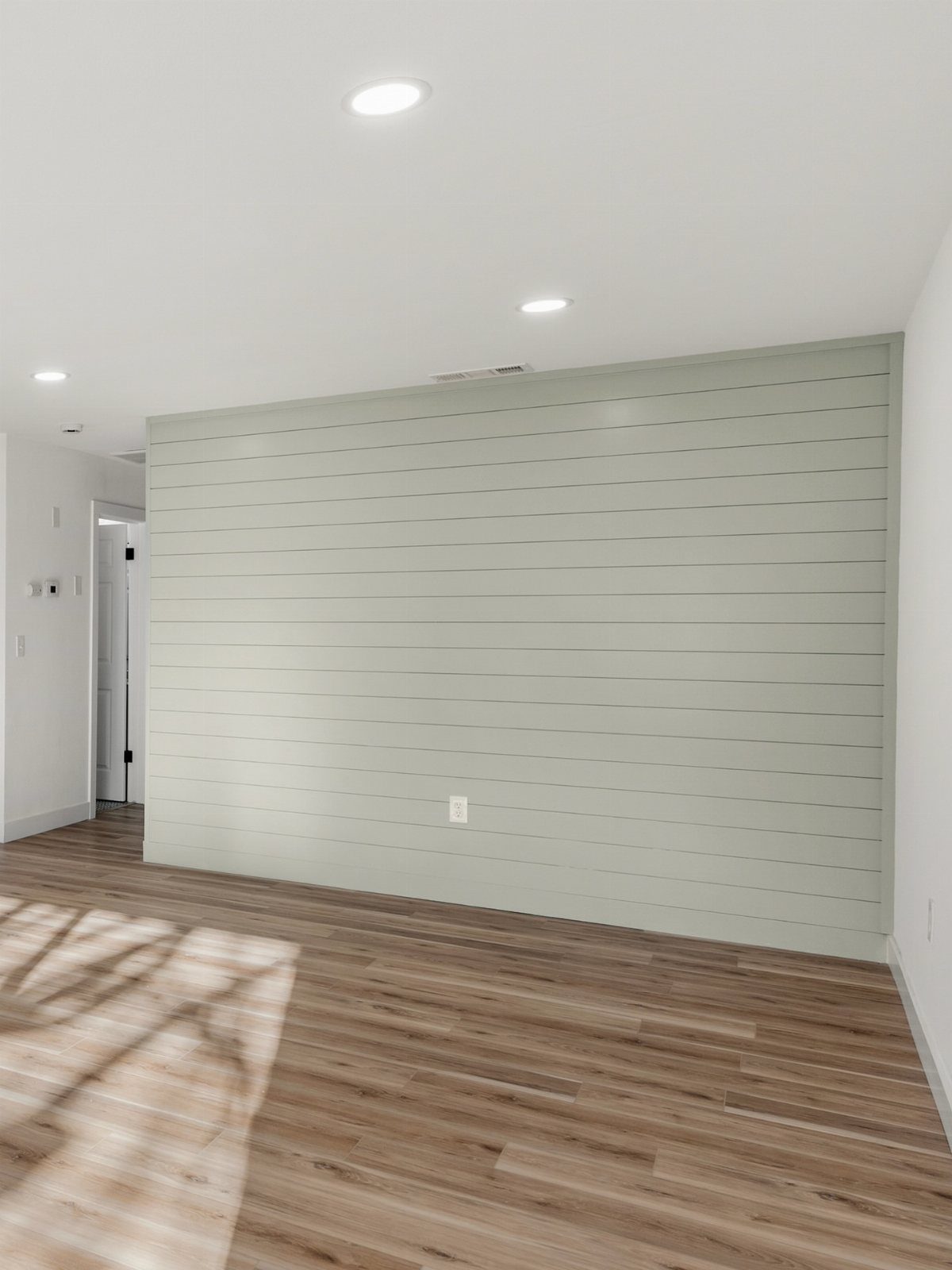 Horizontal sage green shiplap planks installed on an accent wall above wood flooring.