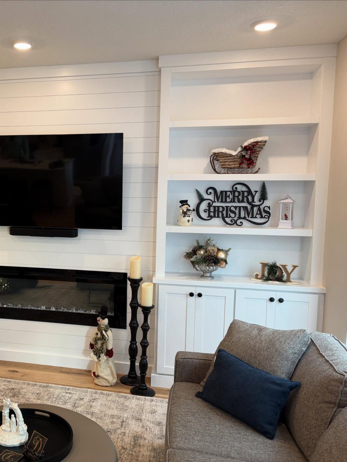 White shiplap accent wall with a television, fireplace, and white built-in shelving unit in a living room.