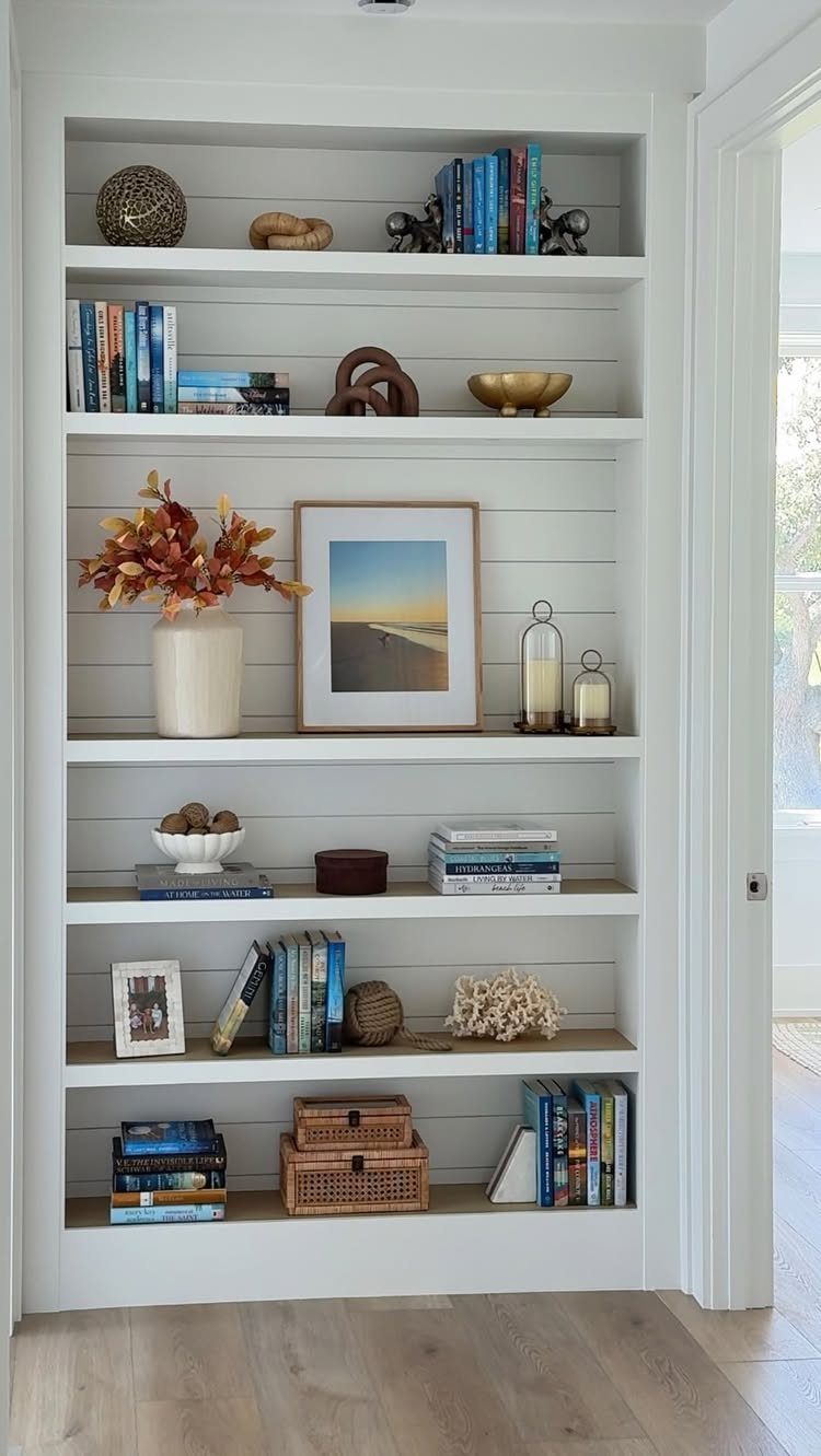 White built-in bookshelves with horizontal shiplap backing decorated with books and decor.