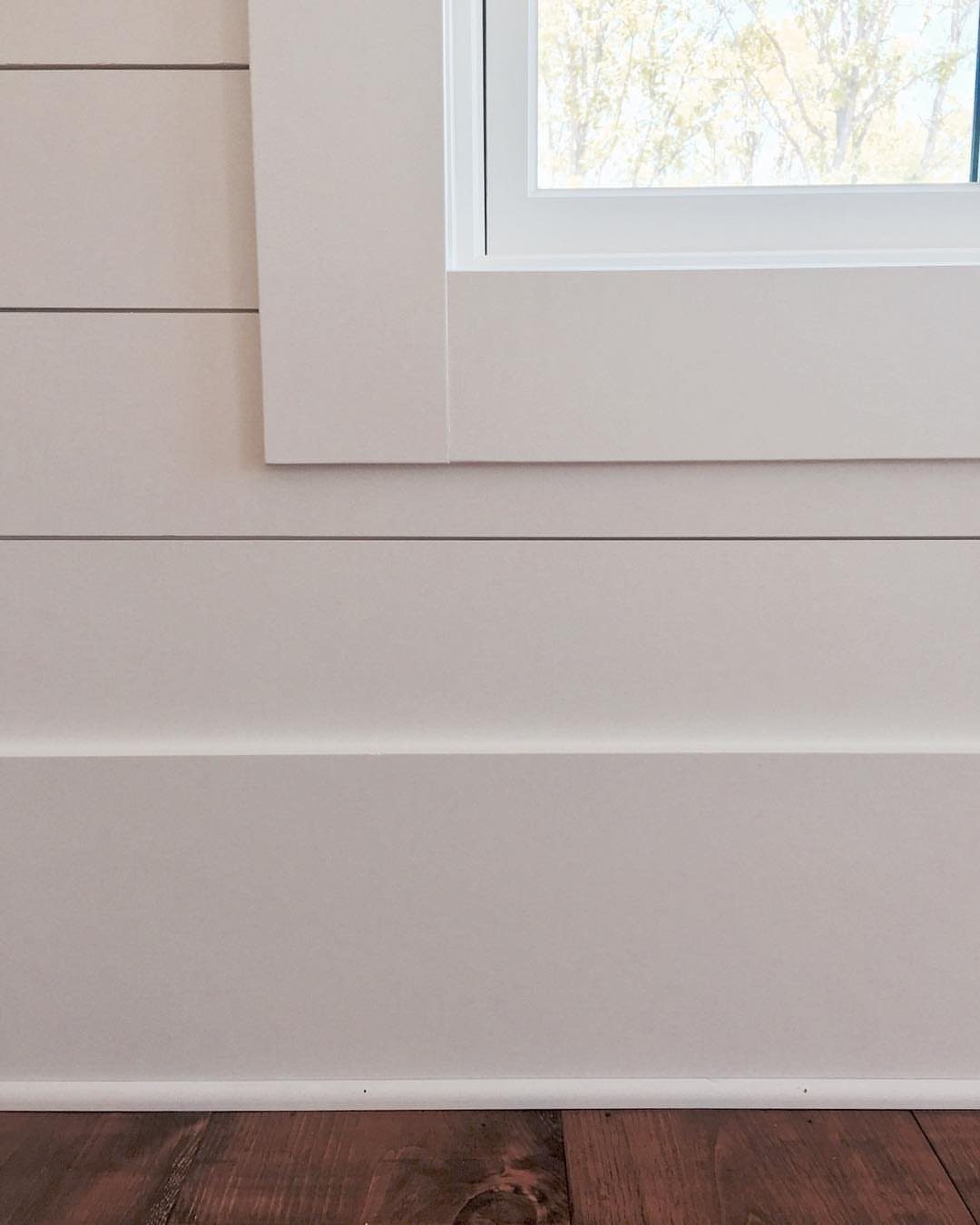 Horizontal light pink shiplap planks on a wall with white window trim and baseboard.