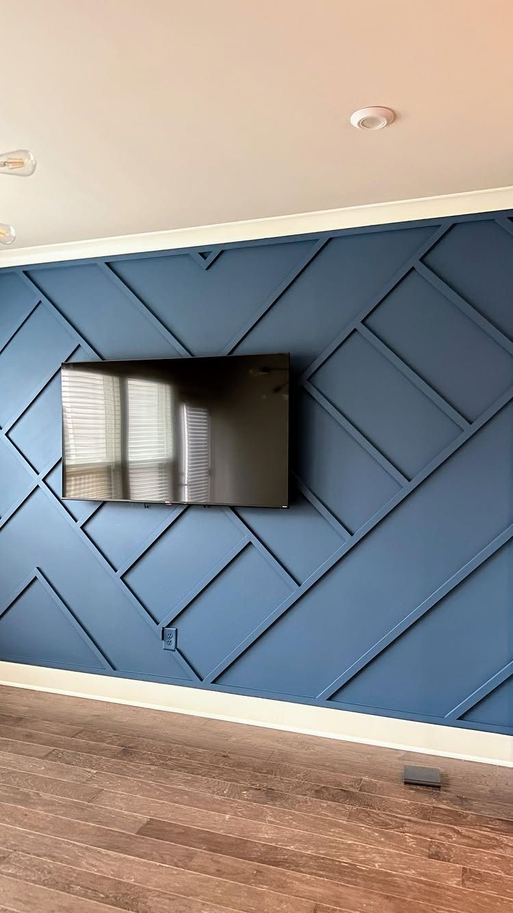 A television mounted on a blue geometric patterned accent wall above a wooden floor.
