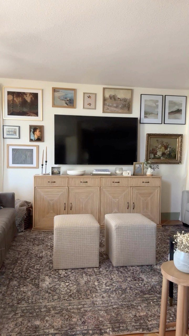 Framed art pieces arranged in a gallery wall around a mounted television above a wooden sideboard.