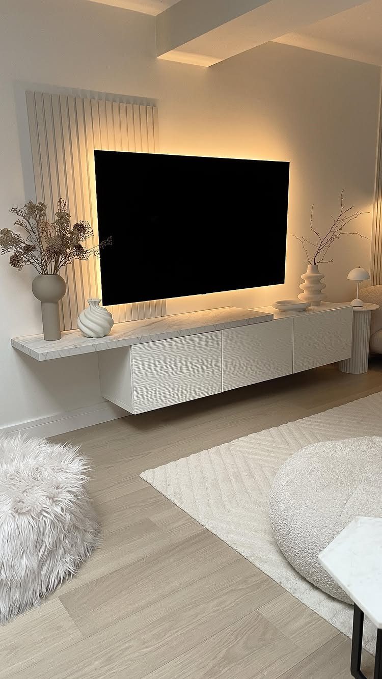 A television mounted on a wall with warm LED backlighting and a white floating console below.