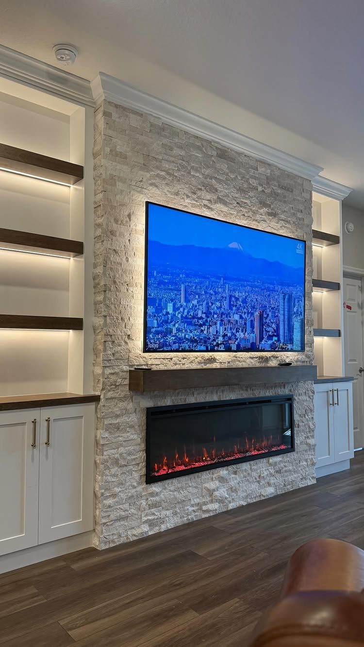 A television mounted on a stone wall above an electric fireplace with built-in shelving.