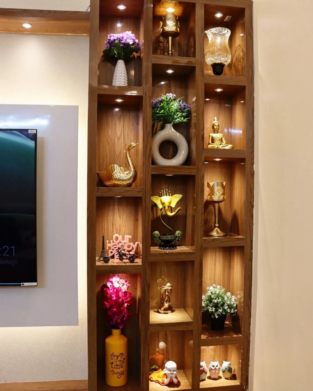 A tall wooden shelving unit filled with various decorative vases, flowers, and golden sculptures under warm lights.
