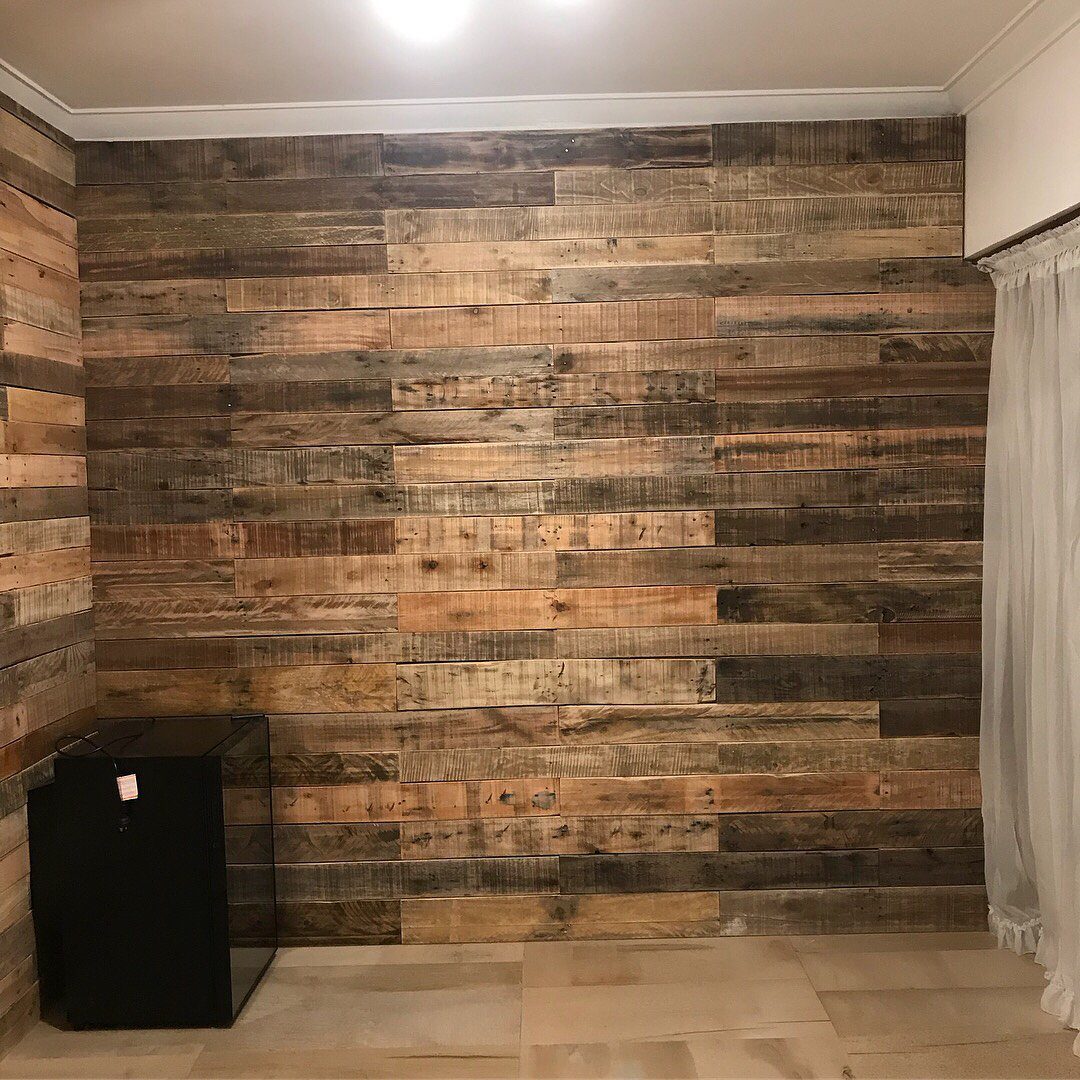 Types of Wall Paneling: 10 Styles for Any Room 6 Reclaimed wood planks in various brown tones covering a wall in a rustic interior setting.