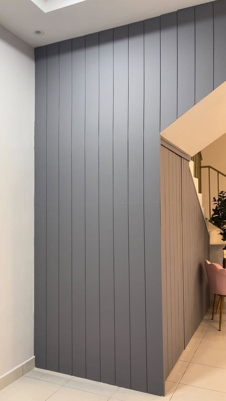Types of Wall Paneling: 10 Styles for Any Room 8 Grey vertical wall paneling installed on a large interior wall near a staircase.