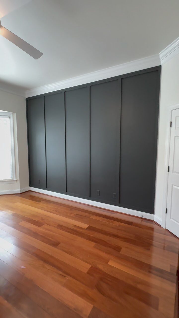 Types of Wall Paneling: 10 Styles for Any Room 7 Dark grey paneled accent wall in a room with hardwood floors and white molding.