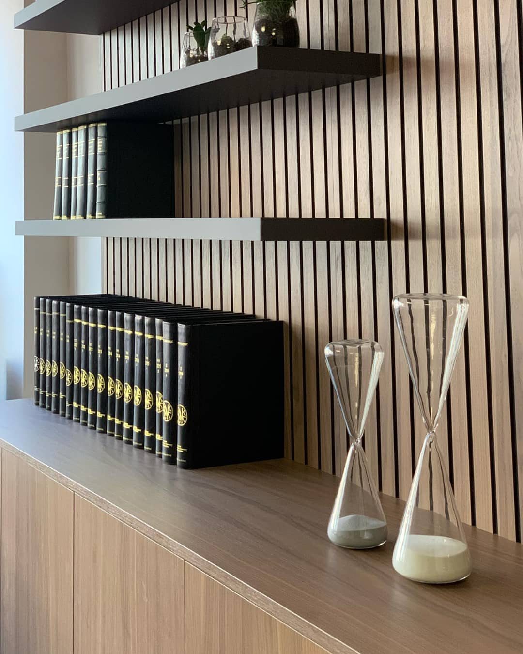 Vertical light wood slats on a wall behind dark floating shelves and books.