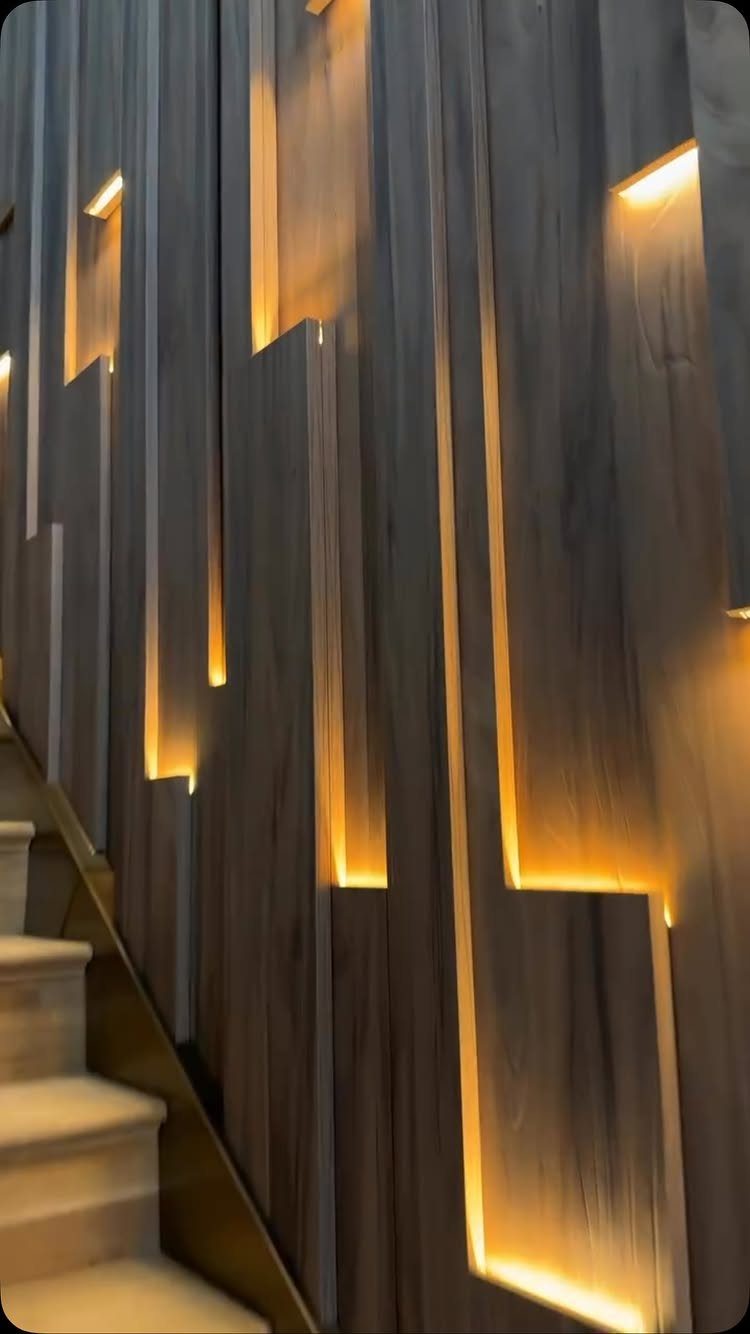 Vertical wooden slats with warm ambient light glowing from behind the panels along a staircase.