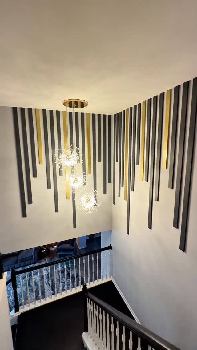Black and gold vertical slats mounted on a white wall in a home staircase area.