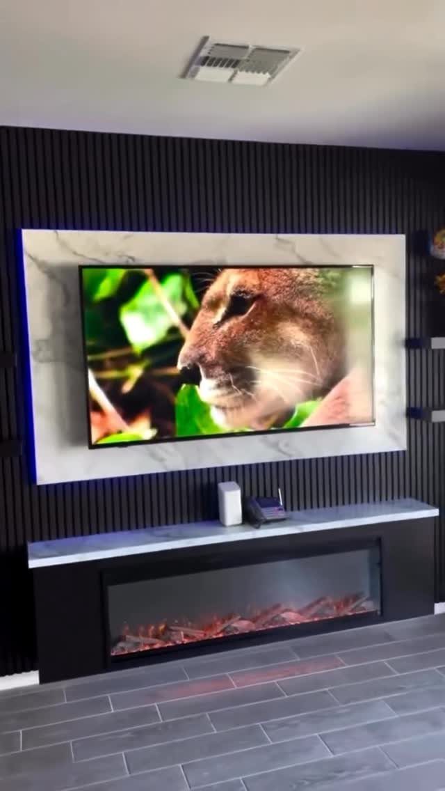 Dark vertical slat wall with a marble TV panel and an electric fireplace below.
