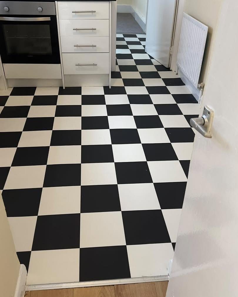 Black and white checkered vinyl flooring installed in a kitchen area next to white cabinets.