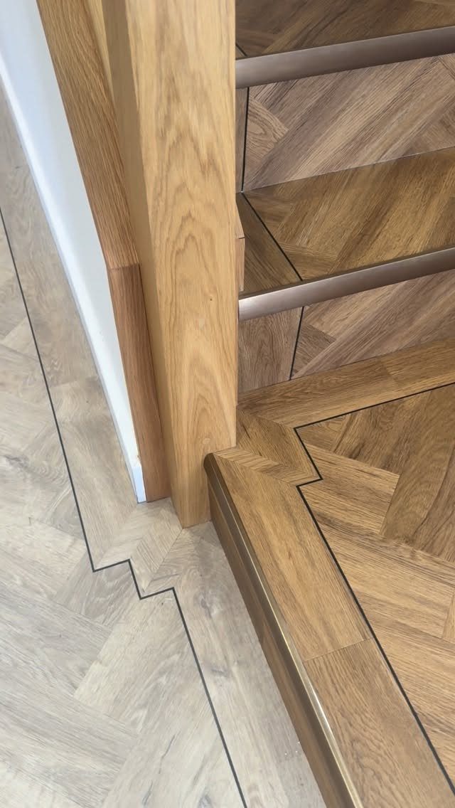 Light wood herringbone vinyl flooring with dark inlay borders meeting a matching staircase.