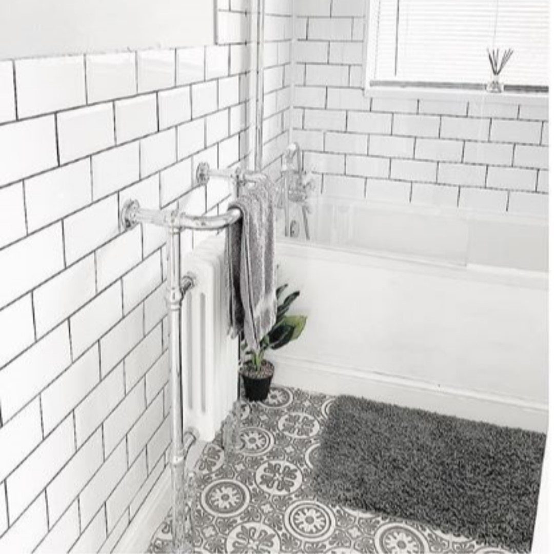 Patterned grey and white vinyl flooring in a white tiled bathroom next to a bathtub.