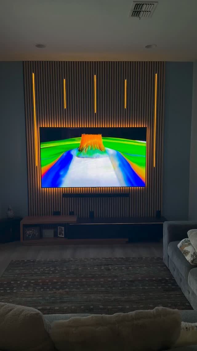 A television mounted on a wood slat wall with glowing yellow LED light strips.