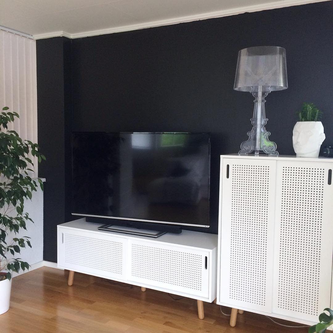A black television mounted on a dark black wall above a white media console.