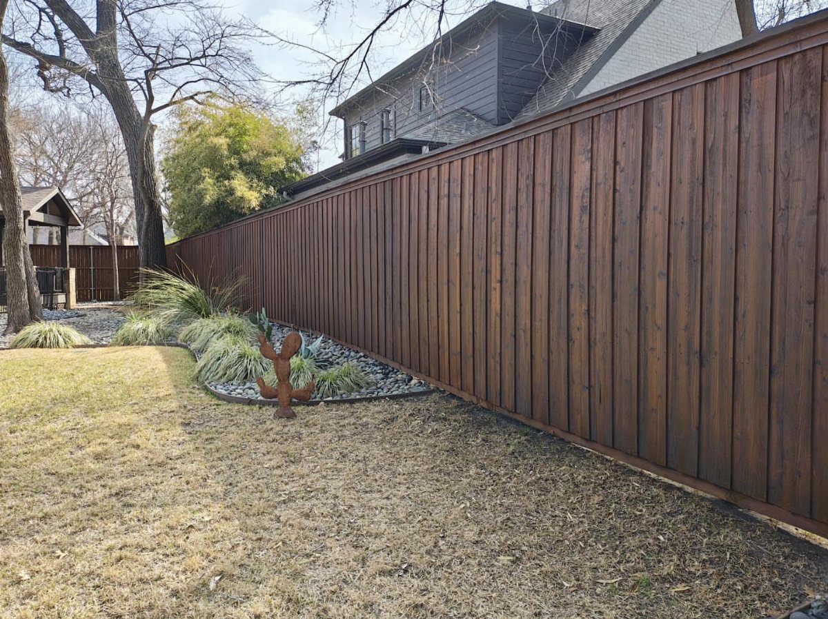 A long dark-stained wooden board-on-board privacy fence bordering a backyard garden.