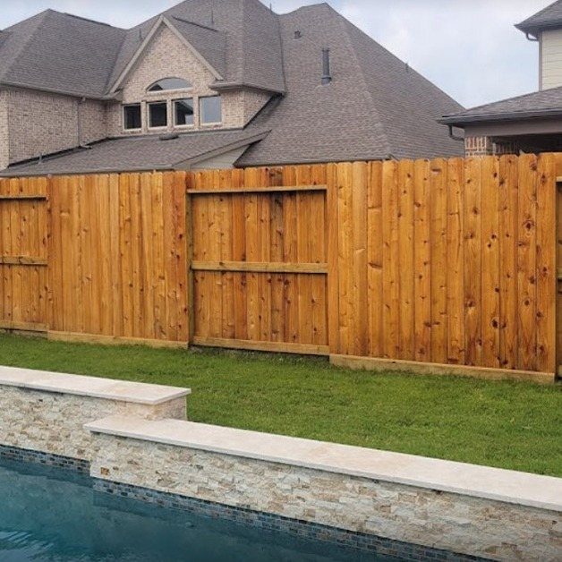 A tall cedar wood fence with a matching gate stands beside a green lawn and pool.