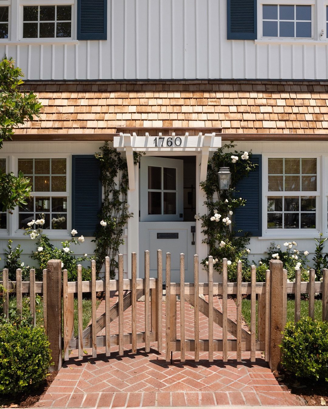 A weathered wooden picket fence with a small gate in front of a white house.