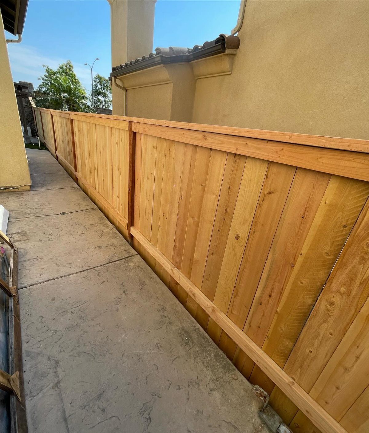 A light wood picture frame fence running alongside a concrete walkway next to a building.