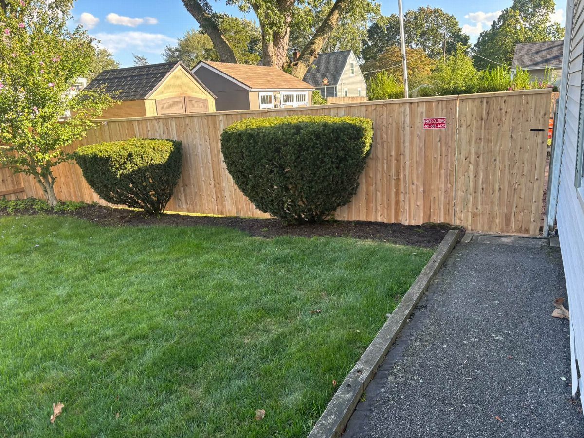 Vertical light wood privacy fence bordering a green lawn and a paved walkway.