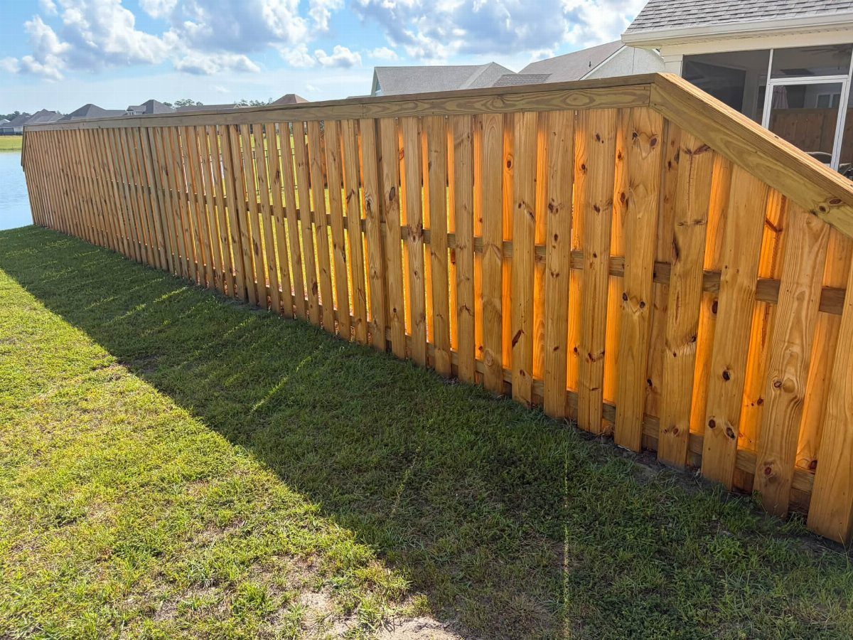 A long wooden shadowbox fence with alternating pickets installed along a green grass lawn.