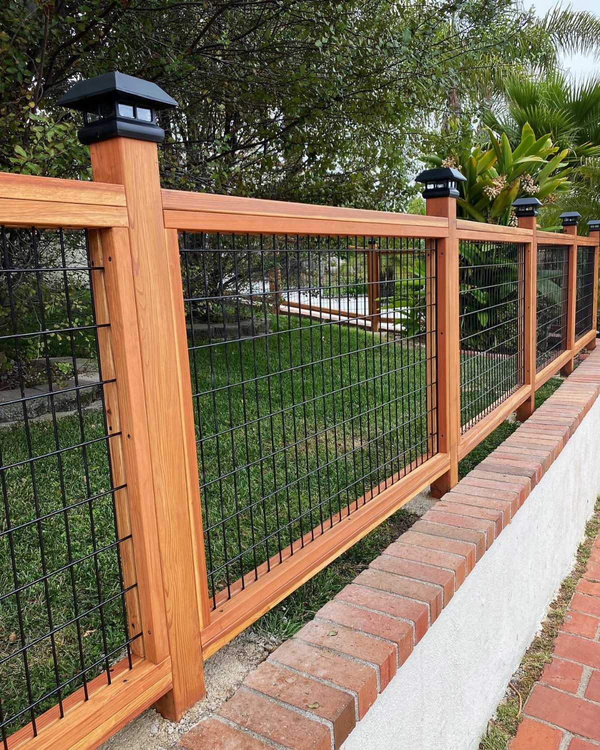 Cedar framed fence with black steel hog wire panels installed along a brick wall.
