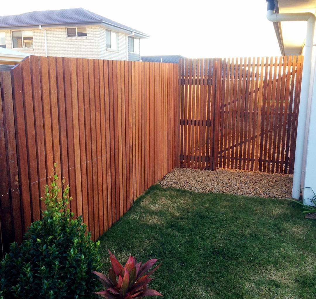 Vertical timber slat fence with a matching gate bordering a green lawn and gravel path.