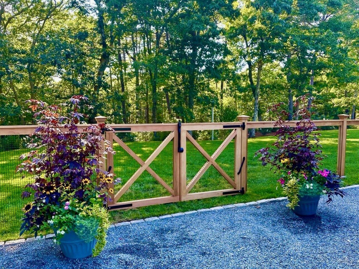 Wooden gate with X-bracing and wire mesh panels set against a backdrop of green trees.