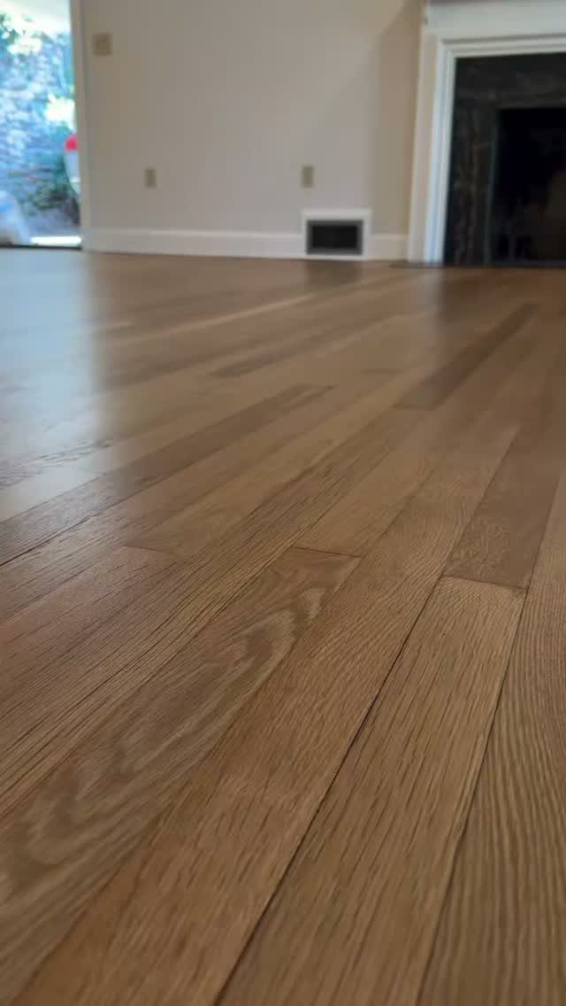 Light brown hardwood floor planks with natural grain extending toward a white wall and doorway.