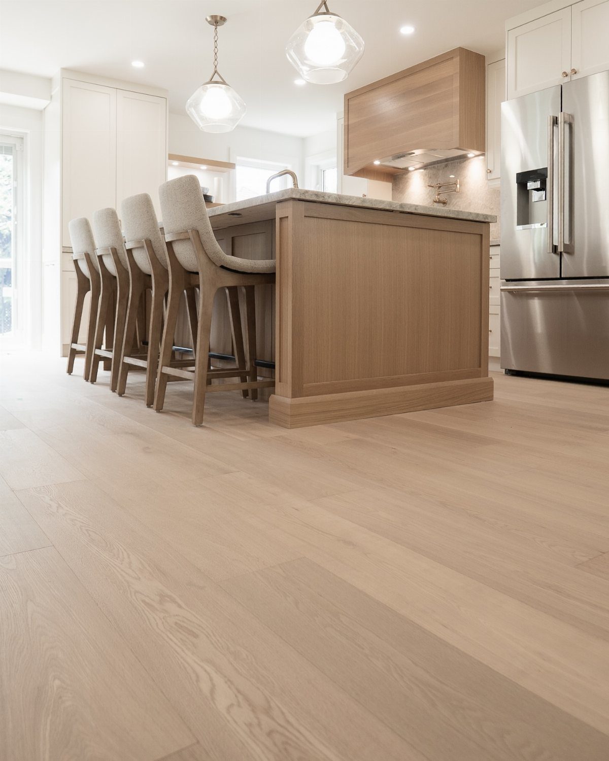 Light wide plank hardwood flooring in a modern kitchen with a wooden island and white cabinets.