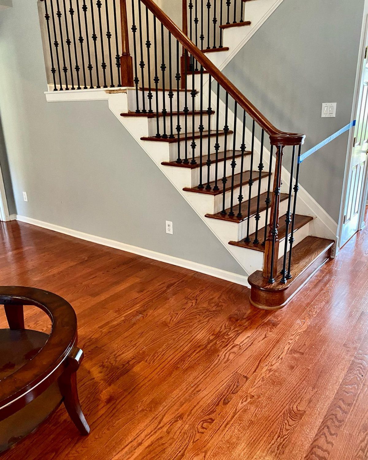 Reddish-brown hardwood floors in a room with a staircase and grey walls.
