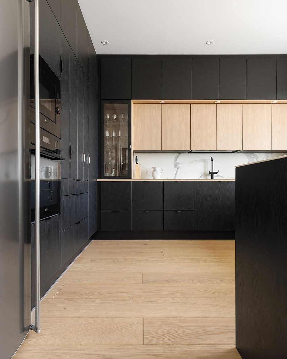 Light wide plank hardwood flooring in a modern kitchen with black and light wood cabinetry.
