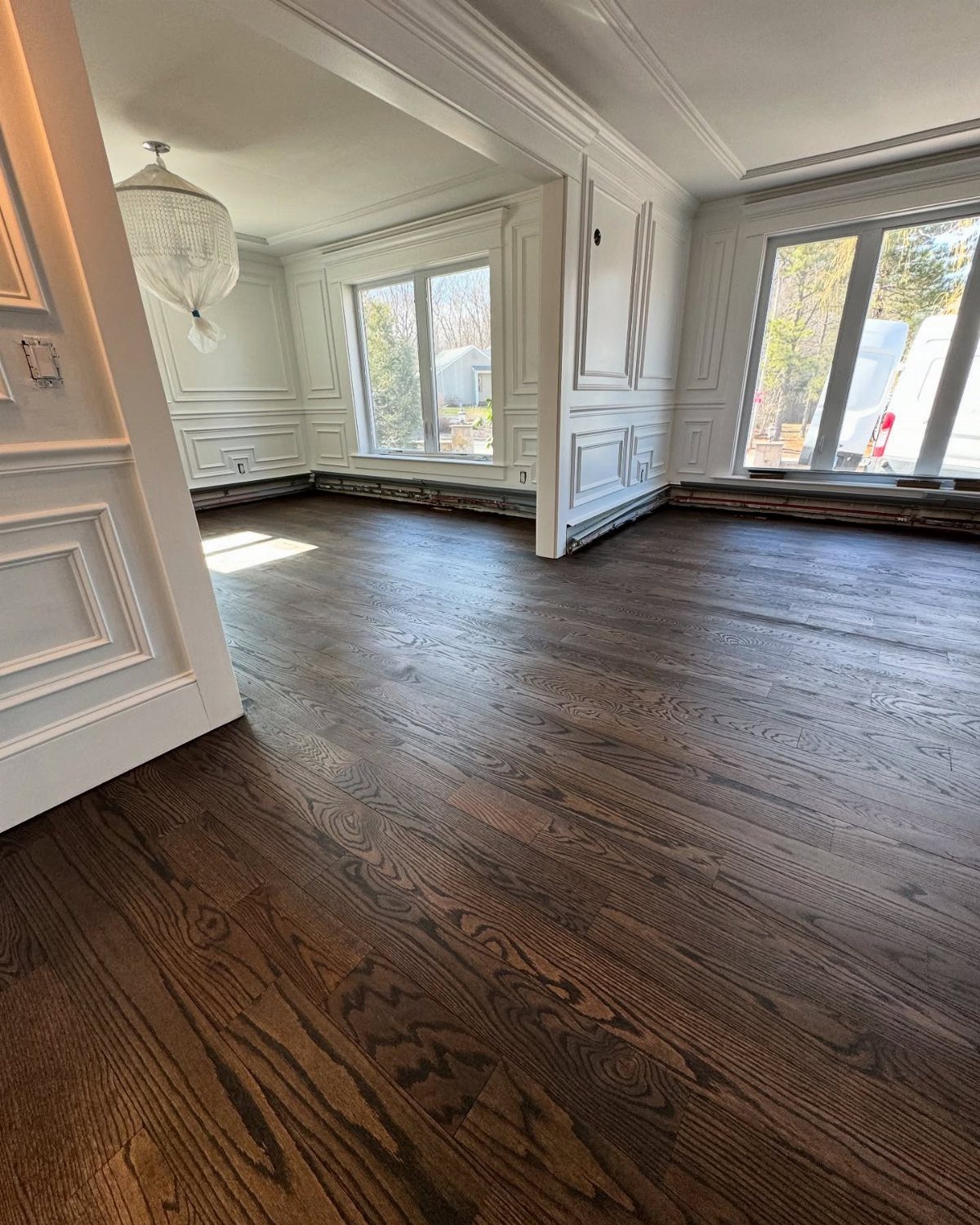 Dark brown wood plank flooring in an empty room with white paneled walls and large windows.